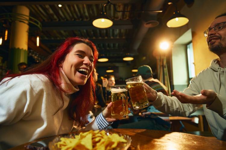 Woman laughing while holding a beer and cheering it with a friend